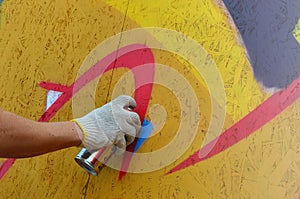 A hand with a spray can that draws a new graffiti on the wall