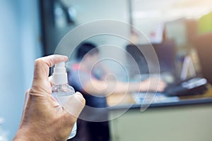 Hand is spraying alcohol with blurry businessman working in office