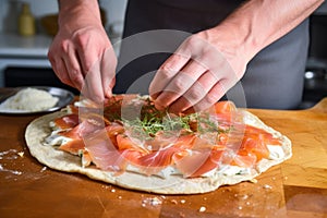 hand spreading cold smoked salmon on homemade pizza dough