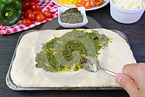 Hand spreading pesto sauce on the pizza dough before baking photo