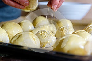 Hand sprinkles sesame seeds onto fresh buns