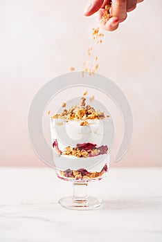 Hand sprinkling granola over healthy raspberry yogurt parfait in