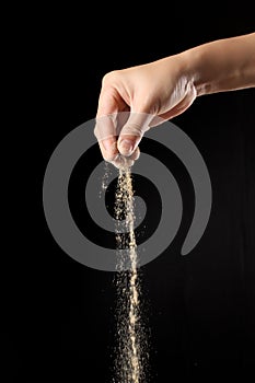 Hand sprinkling ground pepper on black background