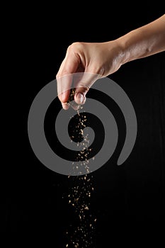 Hand sprinkling oregano on black background