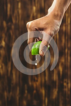 Hand squeeze lime with lime drop on wooden background