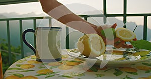 A hand squeezes lemon juice into a cup on a table with a citrus-themed cloth. The table setting reflects a simple