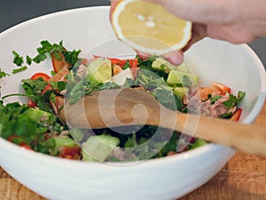 Hand squeezing lemon juice into a bowl of tuna salad.