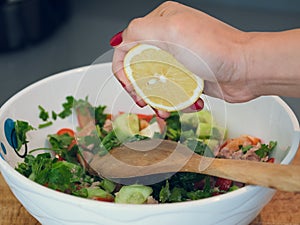 Hand squeezing lemon juice into a bowl of tuna salad.