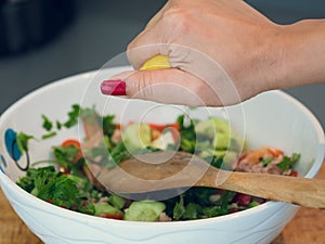 Hand squeezing lemon juice into a bowl of tuna salad.