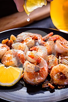 A hand squeezing lemon juice on roasted, grilled shrimp