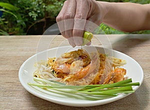 Hand squeezing lemon to Pad Thai stir fried rice noodles with shrimp and egg on plate