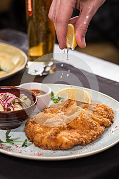 Hand squeezing lemon Weiner Schnitzel with Potatoes and sauce on the table at restaurant