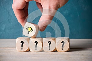 Hand stacking cubes with lightbulb symbol on top of some with questionmarks