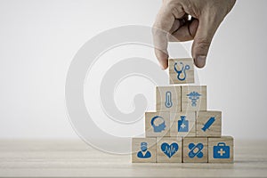 Hand stacking healthcare medicine and hospital icon which printed screen on wooden cubes on table. Health care insurance business