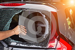 Hand stealing laptop from back side of car which rear glass broken