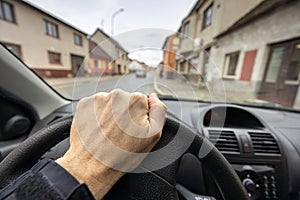 Hand on steering wheel and street with old buildings on background