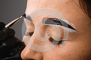 hand in sterile gloves shaping woman eyebrows and applying paint on it using brush. Close-up