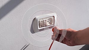 hand sticks orange electrical plug into socket on white wall