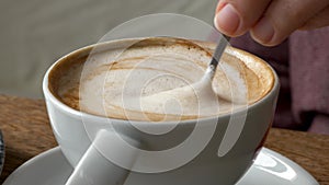 Hand Stirring Cappuccino in a White ceramic Cup on Wooden Tabletop