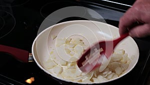 Hand Stirring and Cooking Onion in a Frying Pan with a Red Spoon
