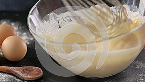 Hand stirring dough with a whisk in glass bowl.