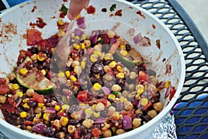 Hand stirring fresh black bean and corn salad in a large serving bowl