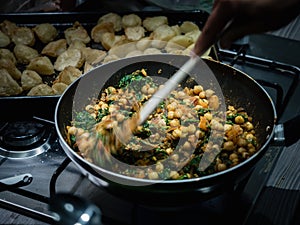 Hand stirring Indian chickpea and spinach curry in wok on gas stove indoors