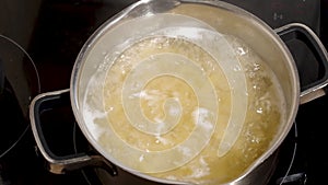 Hand stirring raw pasta boiling in boiling water in a metal pot on the stove, close-up. Homemade food concept