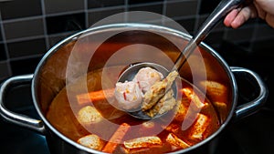 hand stirring up the ingredients to make Oden inside the hot pot using a metal ladle