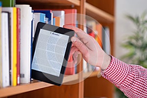 Hand of student keeping digital tablet in bookshelf in school library