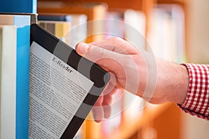 Hand of student keeping digital tablet in bookshelf in school library