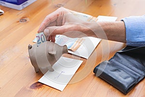 Hand stuffing a bill into a piggy bank for savings. Copy space