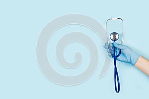 Hand with surgical glove holding a  stethoscope on a light blue background