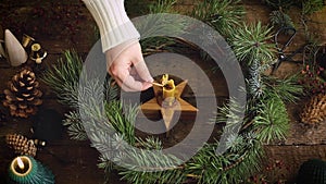 Hand in sweater lighting up candle in christmas wreath on rustic wooden table with pine cones, scissors and decorations. Candle in