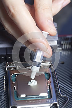 Hand with syringe applying thermal paste on the CPU processor on motherboard