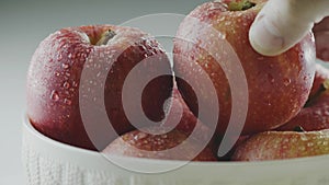 Hand takes eco natural apple in waterdrops from vase, heap of organic red whole fruits, close up studio video