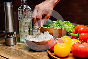 hand takes flour from a wooden bowl and sprinkle a little through his fingers.