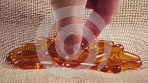 A hand takes a lecithin supplement capsule on a rough rustic burlap napkin close-up.