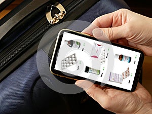 hand takes phone and search medications on travel suitcase background, medical tourism concept, purchase and delivery of medicines
