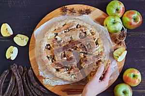 Hand takes a piece of traditional apple pie with spices. Apple tart  decorated with sliced fresh apples, carob pods