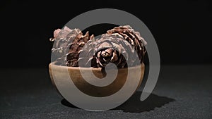 hand takes and puts cedar cone in wooden bowl on black background. Superfood pine nuts.