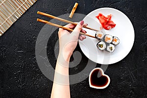 Hand takes sushi roll with salmon and avocado with chopstick. Black background top view