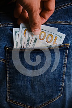 hand takes US dollar banknote from the right front pocket of blue jeans.