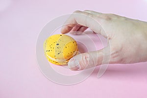 Hand takes yellow macaroon, pink background