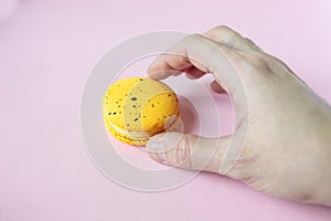 Hand takes yellow macaroon, pink background