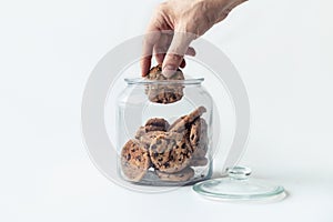 A hand taking cookies from a glass jar on white background