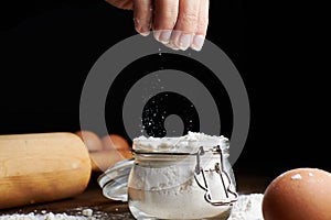 Hand taking flour from a bowl with eggs and a rolling pin on the table