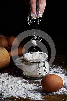 Hand taking flour from a bowl with eggs and a rolling pin on the table