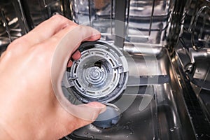 A hand taking out dishwasher filter to clean it, dis washer cleaning concept, kitchen home appliances care and