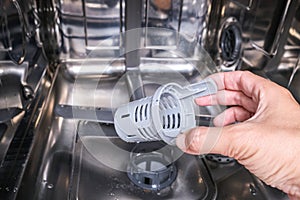 A hand taking out dishwasher filter to clean it, dis washer cleaning concept, kitchen home appliances care and